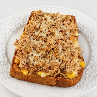 Pão da casa dourado na chapa com manteiga, recheado com frango desfiado, milho cremoso e finalizado com parmesão gratinado