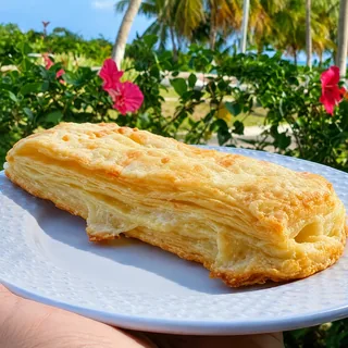 Folhado de queijo dourado servido em prato branco no jardim da Casa Encantada